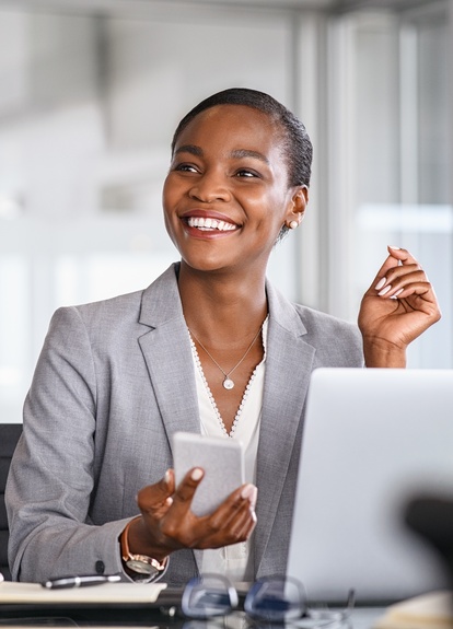 Business Professional Smiling at Desk with Smartphone and Laptop