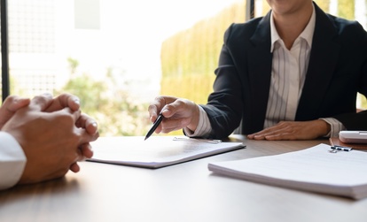 Close-up of two professionals in a business meeting, with one person holding a pen and pointing at a document on a clipboard